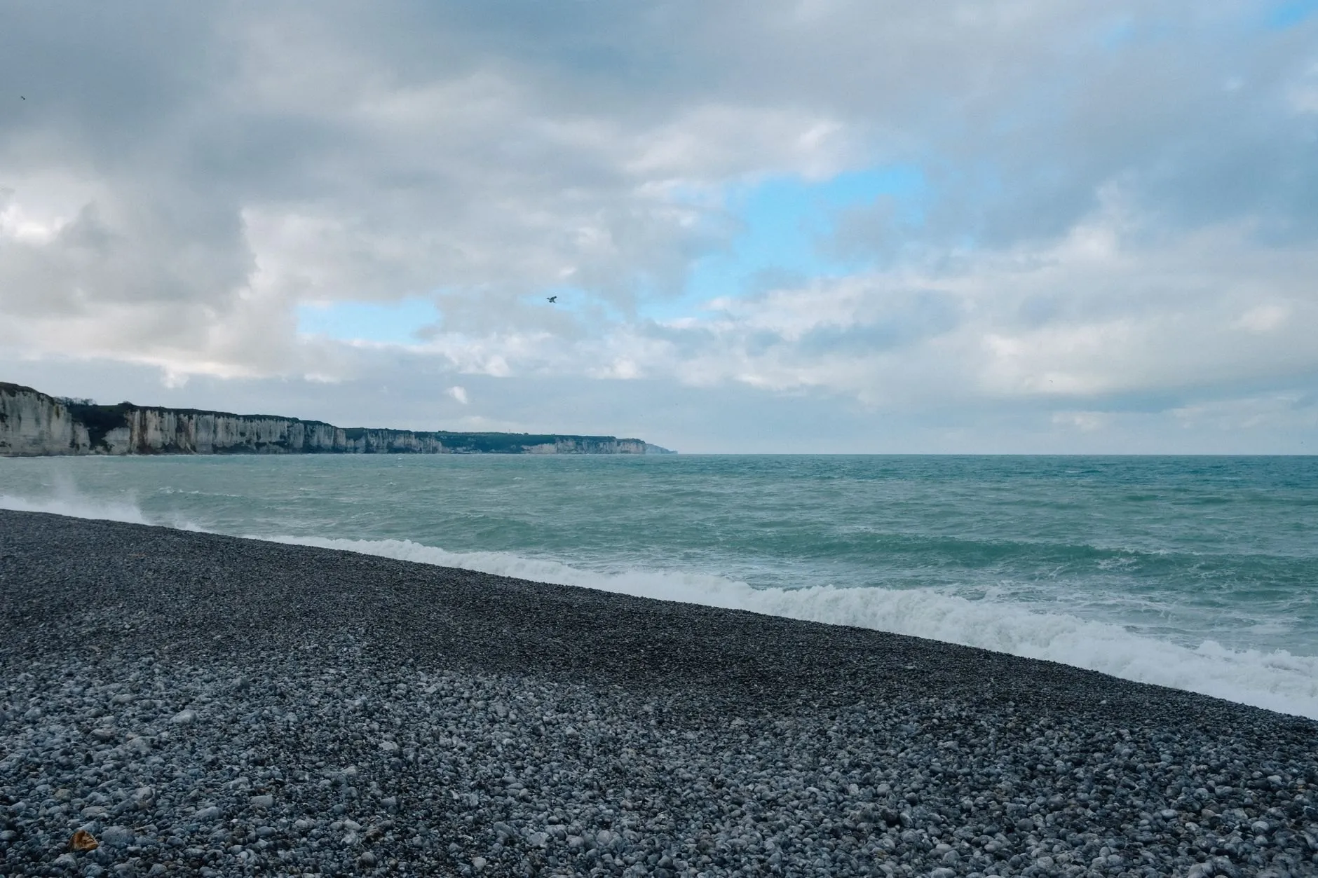 A long shingle beach under white chalk cliffs and a cloudy sky