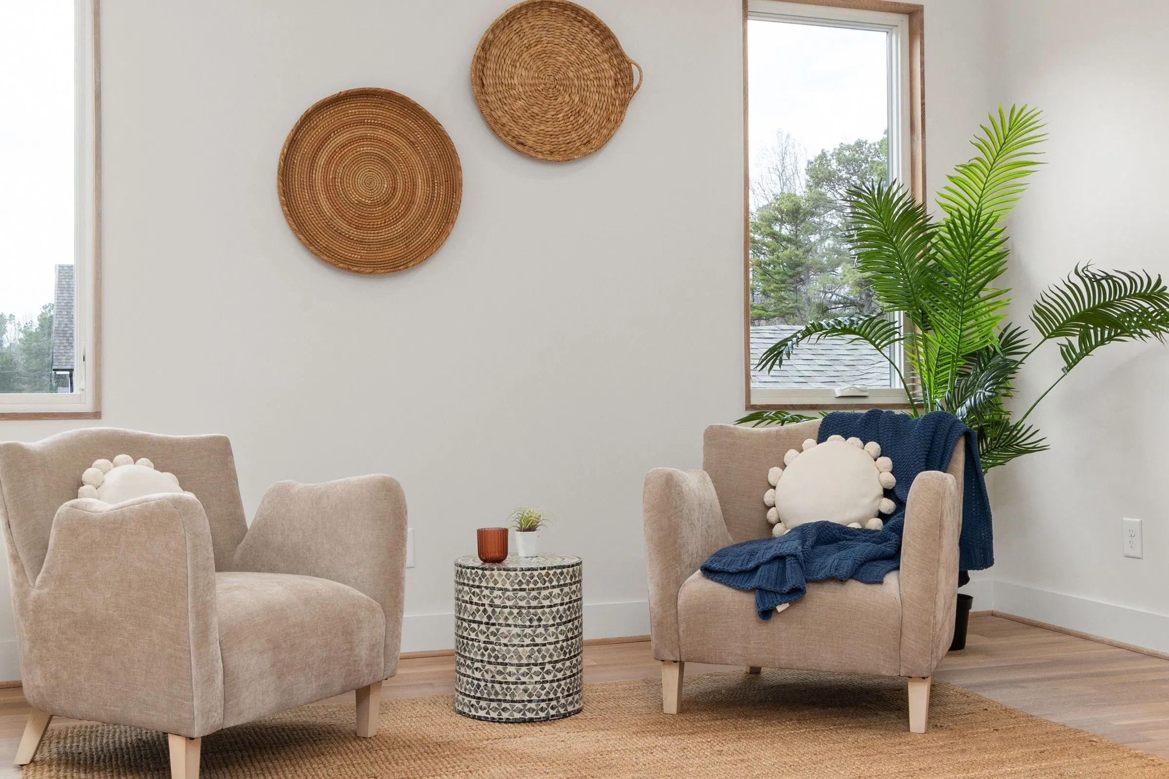 Two soft armchairs facing each other in a bright counselling room with a tall palm and woven wall baskets