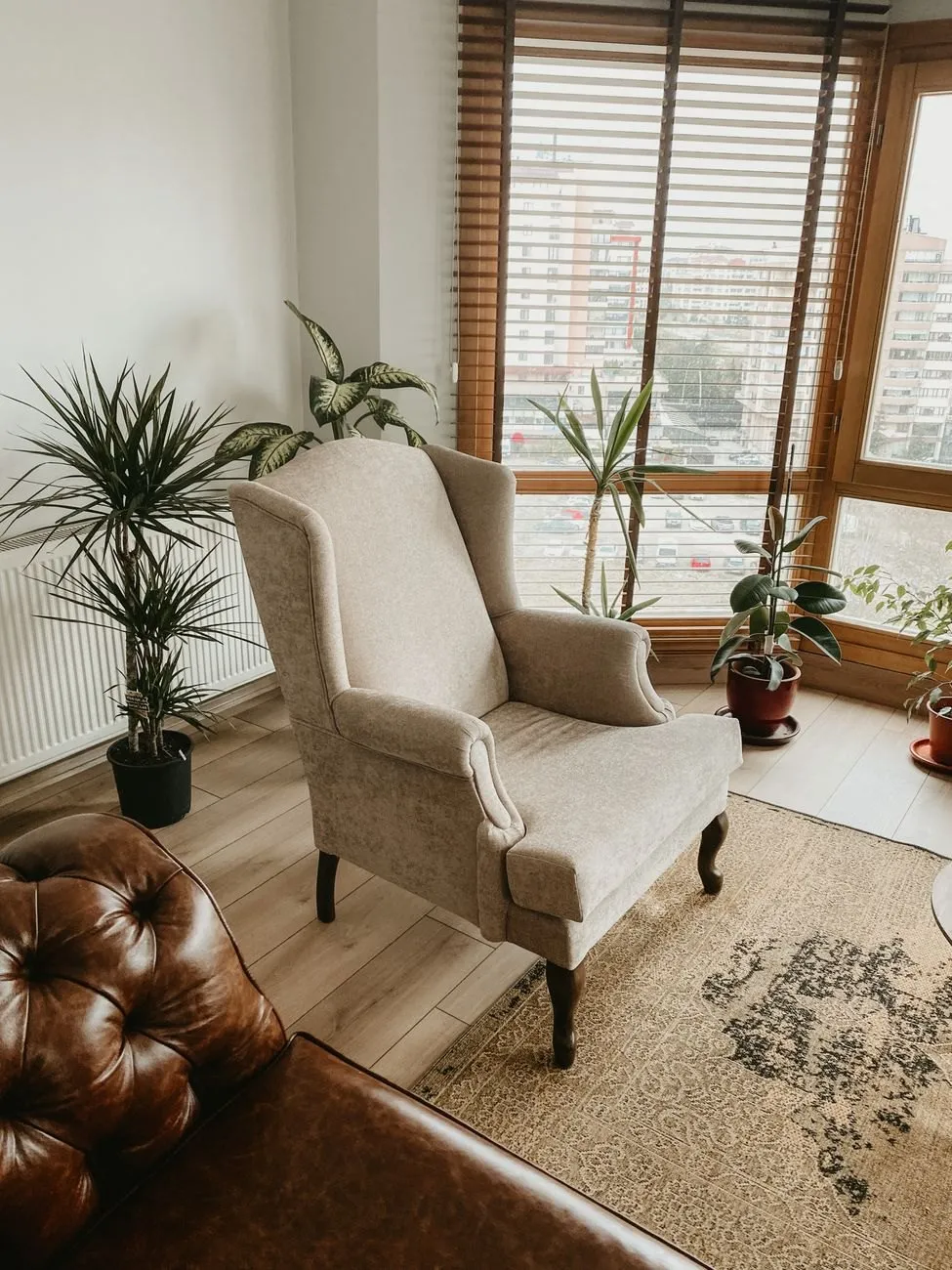 A pale wingback armchair in a bright room with slatted blinds and potted plants