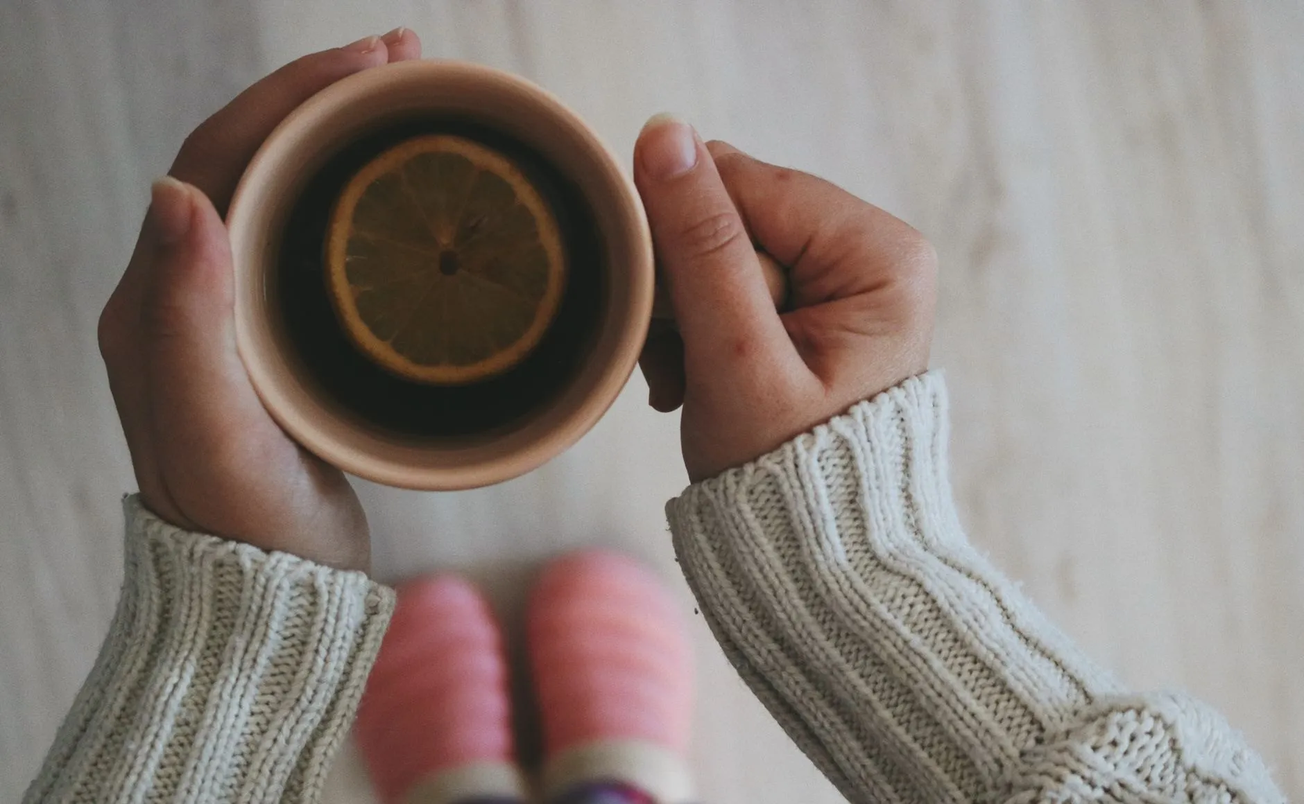 Hands in a cream knitted jumper holding a cup of lemon tea, seen from above